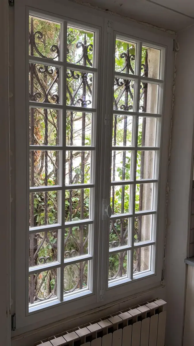 Porte-fenêtre à deux vantaux et petits carreaux, grille en fer forgé côté extérieur