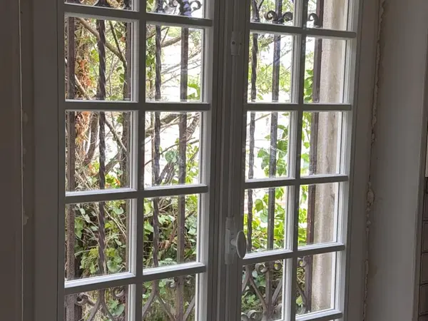 Porte-fenêtre à deux vantaux et petits carreaux, grille en fer forgé côté extérieur