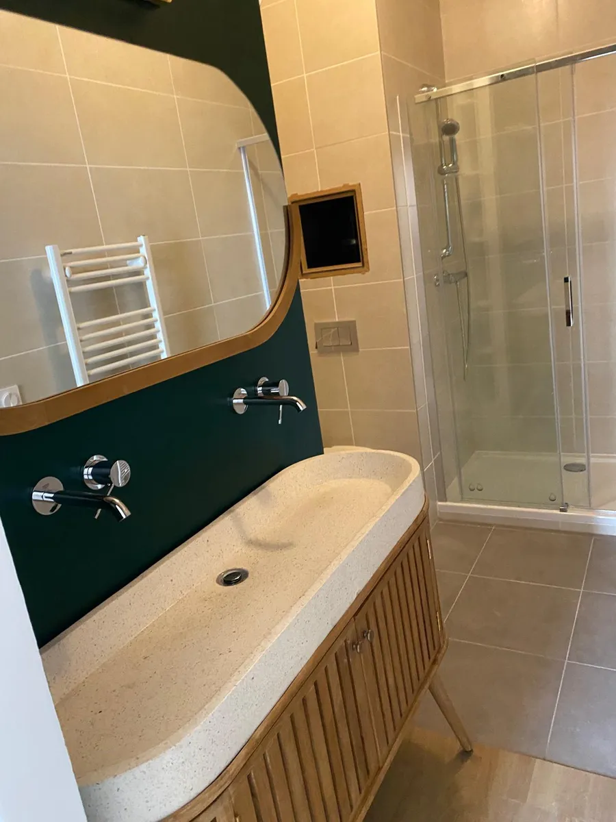 Salle de bain rénovée : vasque sur mur vert, miroir et douche vitrée